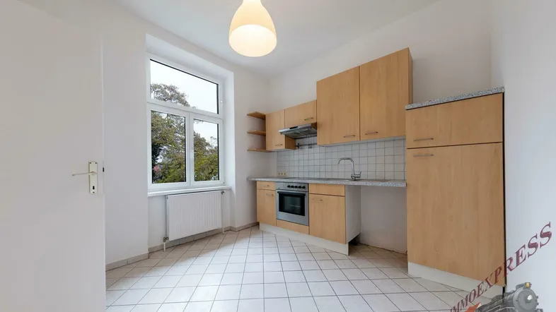 Küche mit hellen Holzschränken, Fliesenboden und Fenster mit Blick ins Grüne.