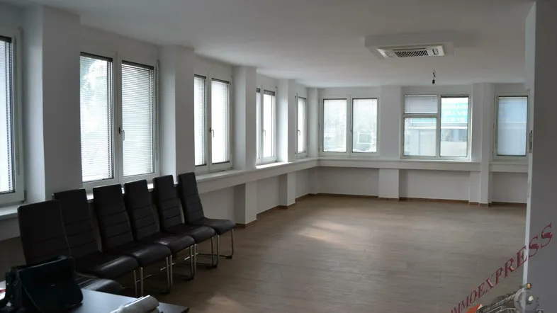 Geräumiger Büroraum mit vielen Fenstern, Jalousien und hellem Laminatboden, ideal für Arbeitsplätze.