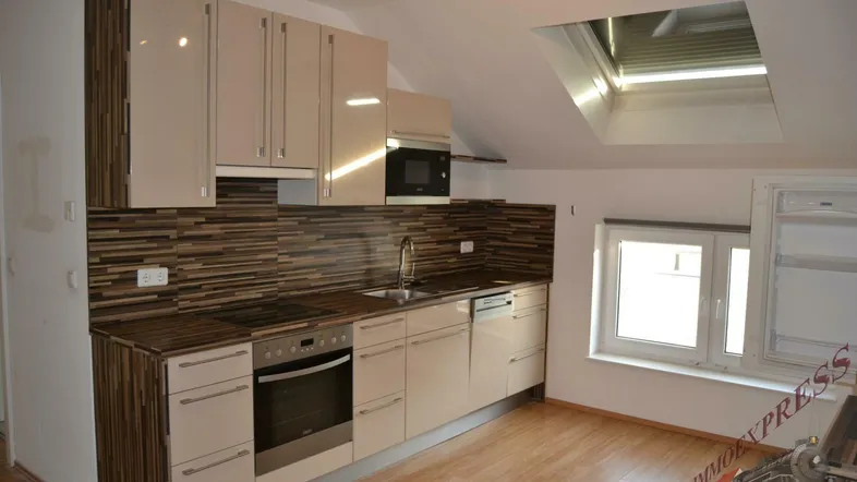 Moderne Küche im Dachgeschoss mit Schrägdachfenster, Einbaugeräten und hellem Laminatboden.