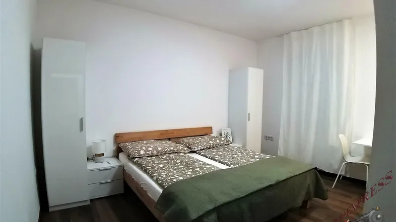 Helles Schlafzimmer mit Holzbett, weißen Schränken und dunklem Holzboden.