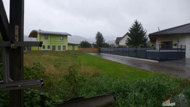 Blick auf ein modernes, hellgrünes Haus mit geschwungenem Dach und Solaranlage, umgeben von Grünflächen und einer Zufahrt.