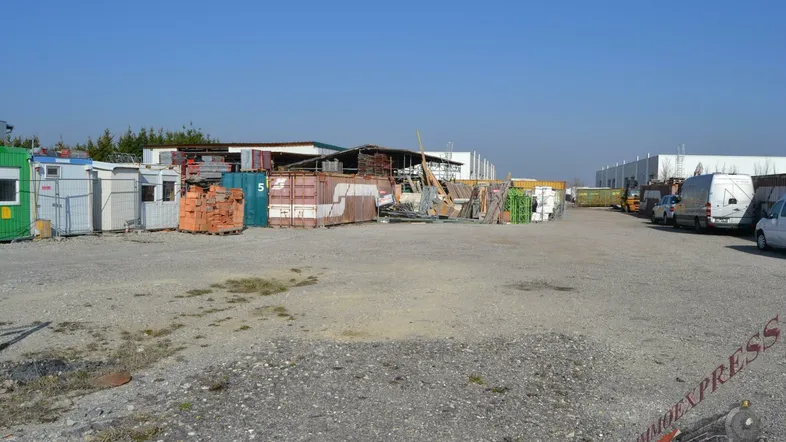Weitläufiges Außengelände mit Lagercontainern, Baumaterialien und Fahrzeugen unter blauem Himmel.