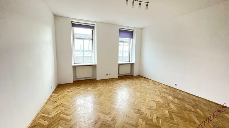 Helles Wohnzimmer mit Fischgrätparkett, weißen Wänden und zwei Fenstern.