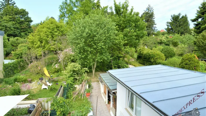 Blick von oben auf den grünen Gartenbereich mit Bäumen, Sträuchern und einem kleinen Spielbereich.