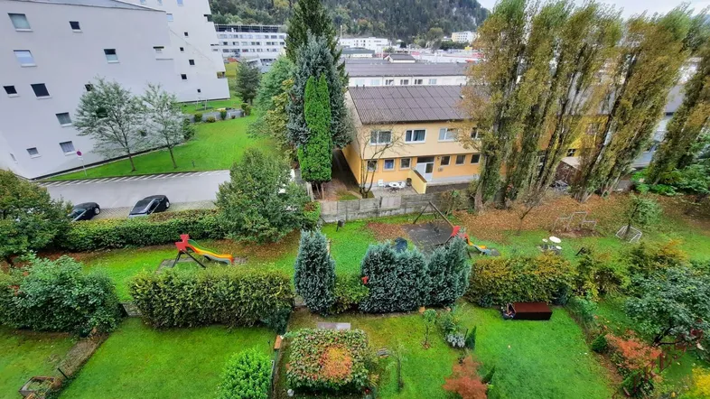 Blick auf die Wohnanlage mit Grünflächen, Spielplatz und umliegenden Bergen.