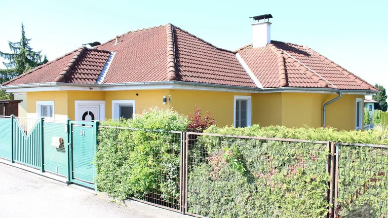 Gelbes Einfamilienhaus mit rotem Ziegeldach, grüner Hecke und Vorgarten.