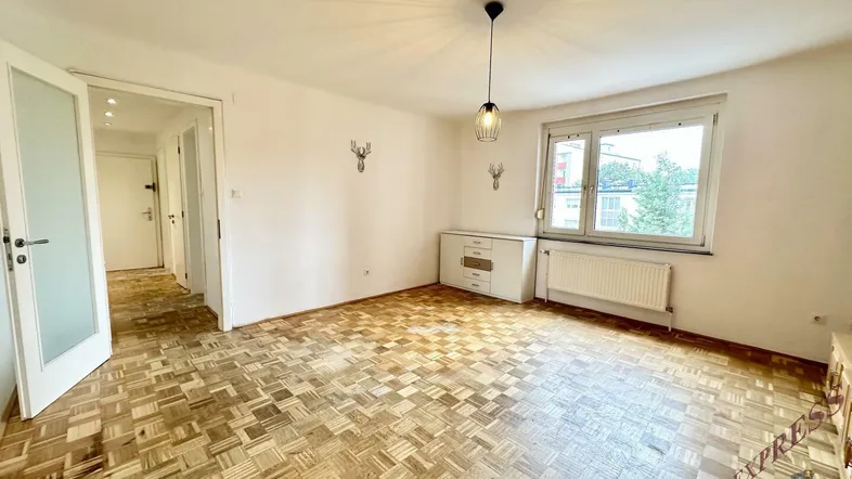 Heller Wohnraum mit charakteristischem Parkettboden, großem Fenster und Blick ins Grüne, ideal für individuelle Gestaltung.