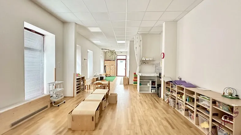 Heller, langer Raum mit Holzfußboden und Kindermöbeln, ideal als Spielzimmer oder Klassenzimmer.
