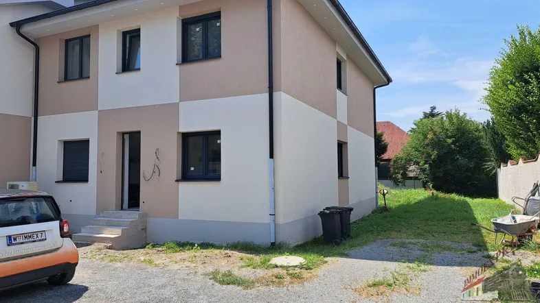 Neubau-Doppelhaushälfte mit beiger und weißer Fassade, großen Fenstern und kleinem Vorgarten.