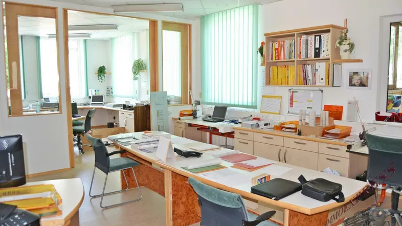 Geräumiges Büro mit mehreren Arbeitsplätzen, Holzmöbeln und viel Tageslicht durch große Fenster.