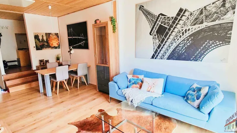 Geräumiger Wohn-Essbereich mit Holzboden, bequemer Couch und Esstisch, dekoriert mit Kunstwerken an den Wänden.