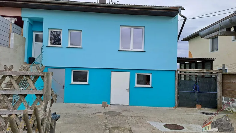 Modernes Haus mit leuchtend blauer Fassade, mehreren Fenstern und einem gepflasterten Hofbereich.