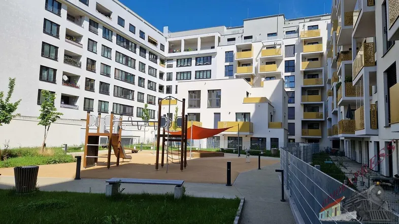 Moderner Wohnkomplex mit weißer Fassade, gelben Balkonen und einem Spielplatz im Innenhof.