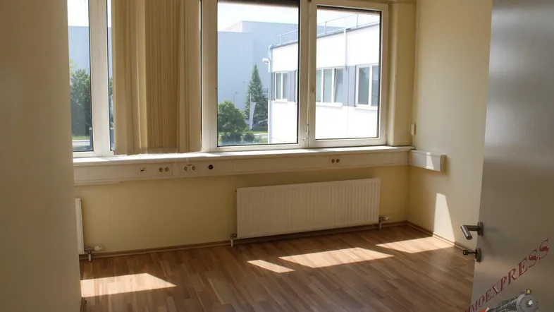Heller Büroraum mit Laminatboden und großen Fenstern, die viel Tageslicht hereinlassen.
