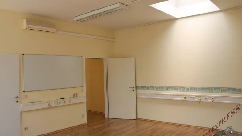 Heller Büroraum mit Laminatboden, Klimaanlage, Whiteboard und vielen Steckdosenleisten an den Wänden.