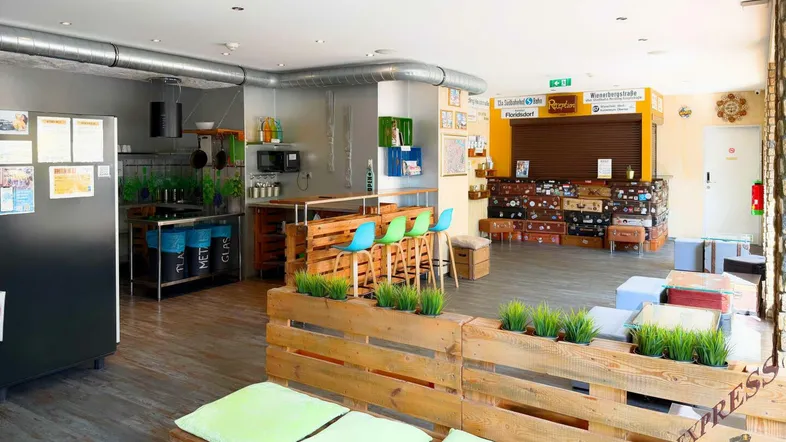 Großer Gemeinschaftsbereich mit einer Bar aus Holzpaletten, einer kleinen Küche und verschiedenen Sitzgelegenheiten.