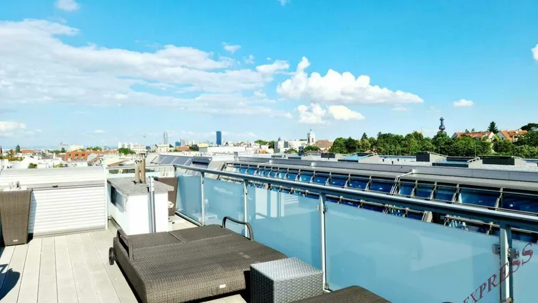 Geräumige Dachterrasse mit Liegestühlen und weitem Blick über die Stadt unter blauem Himmel.