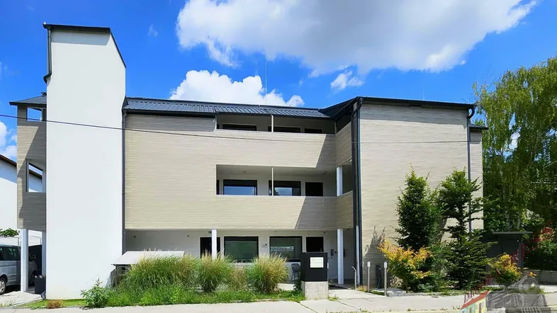 Modernes Mehrfamilienhaus mit heller Fassade und Balkonen unter blauem Himmel.