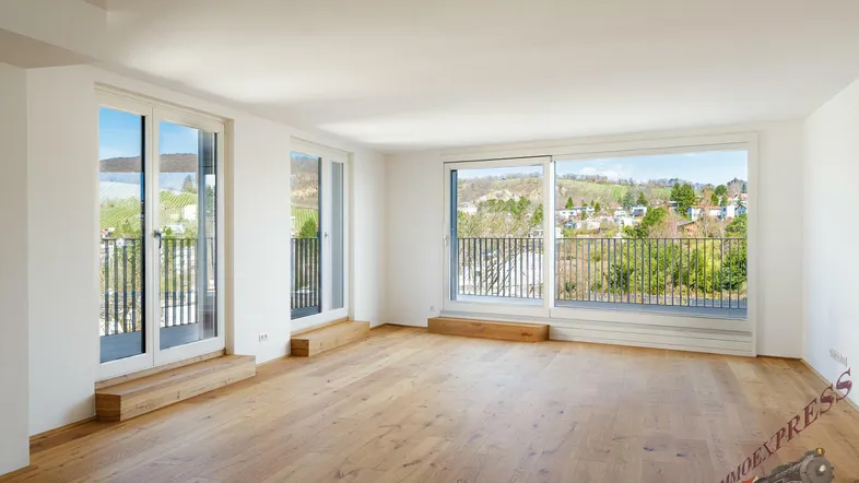 Helles Wohnzimmer mit Holzboden und Zugang zu mehreren Balkonen mit Weitblick.
