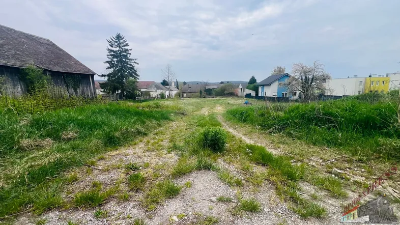 Weitläufiges Grundstück mit Gras und Schotterweg, umgeben von ländlicher Bebauung unter bewölktem Himmel.