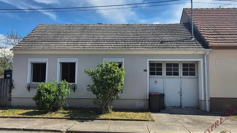 Einfaches Einfamilienhaus mit Garage und Satteldach, umgeben von einer kleinen Grünfläche.