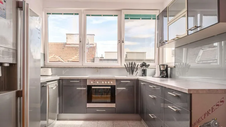 Moderne Küche mit grauen Hochglanzfronten, Edelstahlgeräten und Blick auf die Dächer der Stadt.