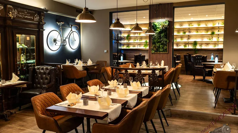 Gemütlicher Restaurantbereich mit dunklen Holzmöbeln, gepolsterten Stühlen und dekorativer Wandgestaltung.