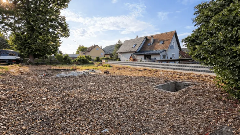 Leeres Grundstück mit Holzspänen und einem Haus im Hintergrund unter blauem Himmel.