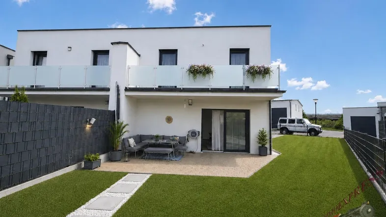 Moderne Reihenhausfassade mit privater Terrasse, kleinem Garten und Balkon im Obergeschoss.
