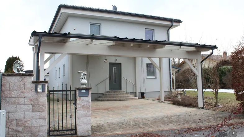 Modernes Einfamilienhaus mit heller Fassade, Carport und gepflasterter Auffahrt im Vorgartenbereich.