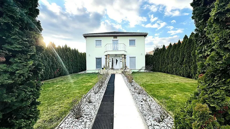 Elegantes Einfamilienhaus mit gepflegtem Vorgarten, umgeben von hohen Hecken und einem stilvollen Weg.