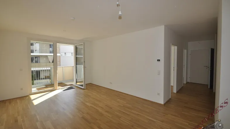Helles Wohnzimmer mit Parkettboden und Zugang zu einem sonnigen Balkon.