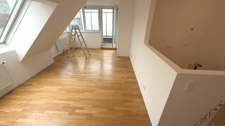 Heller Dachgeschossraum mit Holzboden, Dachfenstern und Zugang zu einem kleinen Außenbereich.