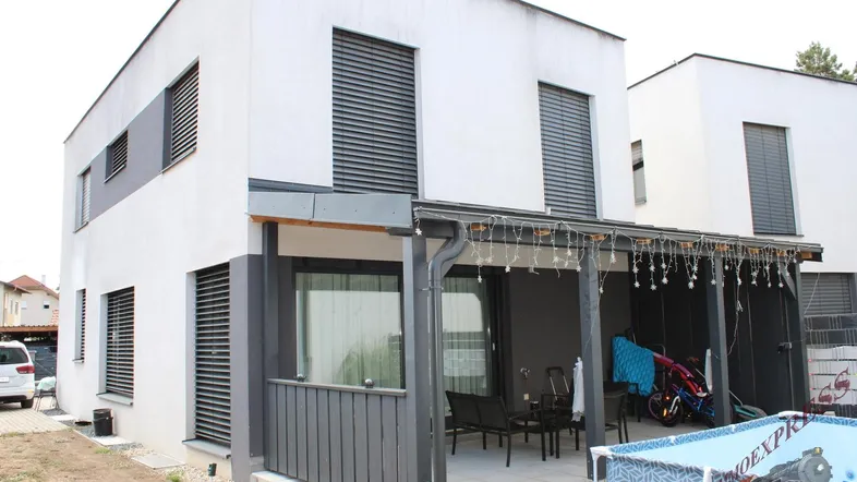 Moderne Hausfassade mit überdachter Terrasse, Sitzgelegenheiten und Spielbereich im Freien.