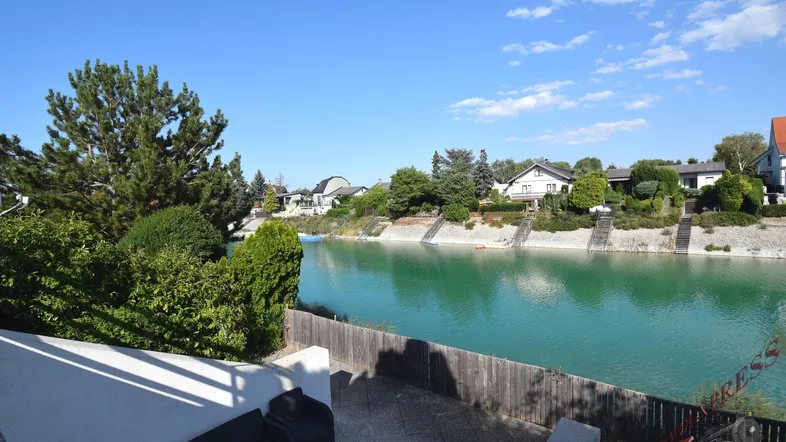 Sonnige Terrasse mit modernen Gartenmöbeln und direktem Blick auf den See und die gegenüberliegenden Häuser.