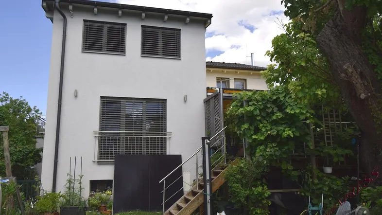 Ansicht des modernen Hauses von der Gartenseite mit Außentreppe und grüner Umgebung.