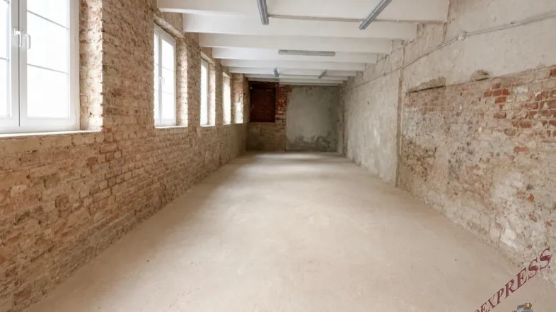 Langer, leerer Raum mit unverputzten Ziegelwänden, Betonboden und mehreren Fenstern, ideal für Lager oder Werkstatt.