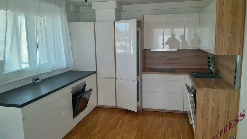 Moderne Küche mit weißen Hochglanzfronten, Holzelementen und Parkettboden, ausgestattet mit Backofen und Geschirrspüler.