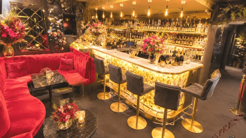Luxuriöse Bar mit rotem Samtsofa, beleuchteter Theke und einer großen Auswahl an Getränken.