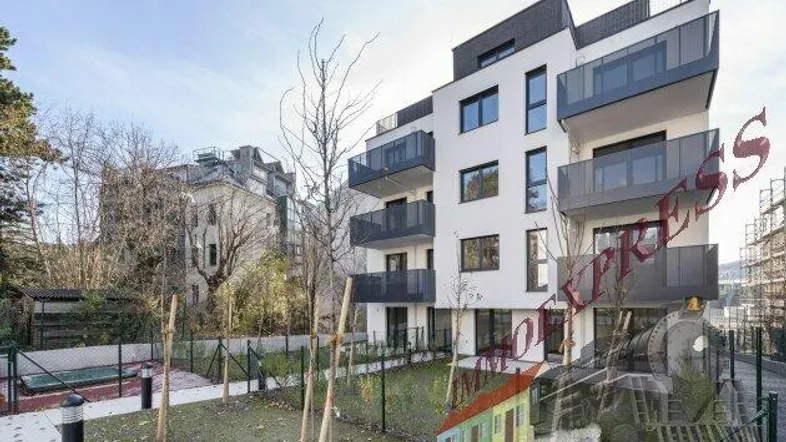 Modernes Mehrfamilienhaus mit weißen Fassaden, großen Fenstern und Balkonen sowie Grünflächen.