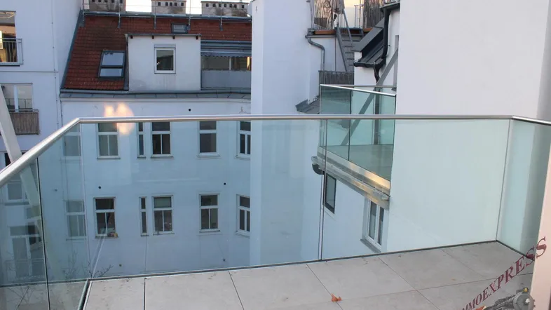 Moderne Terrasse mit Glasgeländer und Blick auf umliegende Gebäude und einen Innenhof.