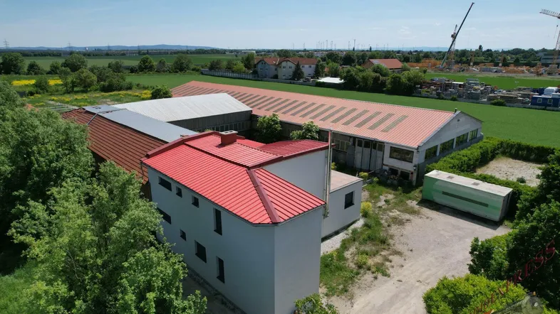 Luftaufnahme eines Anwesens mit mehreren Gebäuden, umgeben von Feldern und Bäumen unter blauem Himmel.