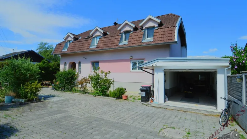 Einfamilienhaus mit gepflasterter Auffahrt, Garage und Gaubenfenstern unter blauem Himmel.