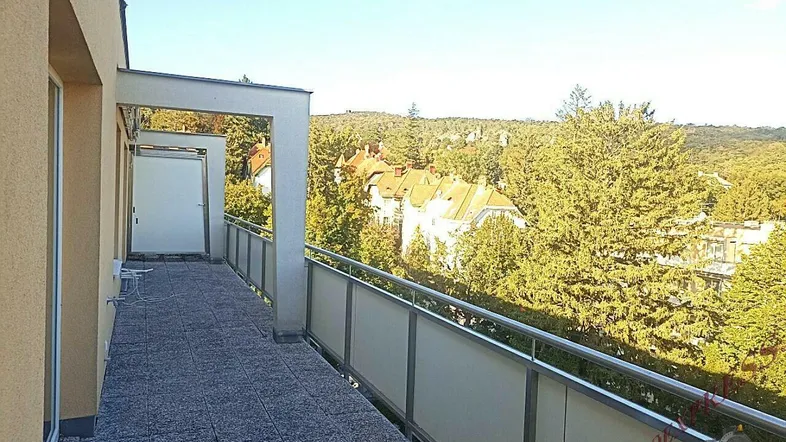 Langer Balkon mit Fliesenboden und weitem Blick ins Grüne und auf umliegende Gebäude.