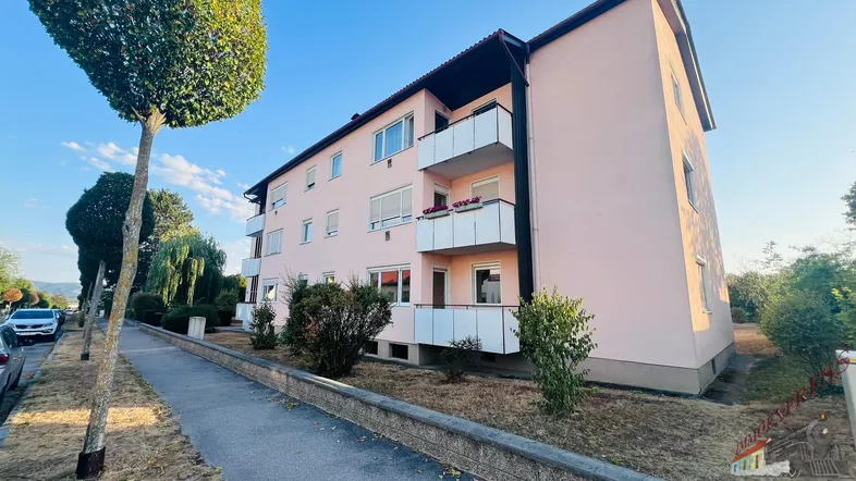 Mehrfamilienhaus mit rosa Fassade und Balkonen an einem sonnigen Tag.