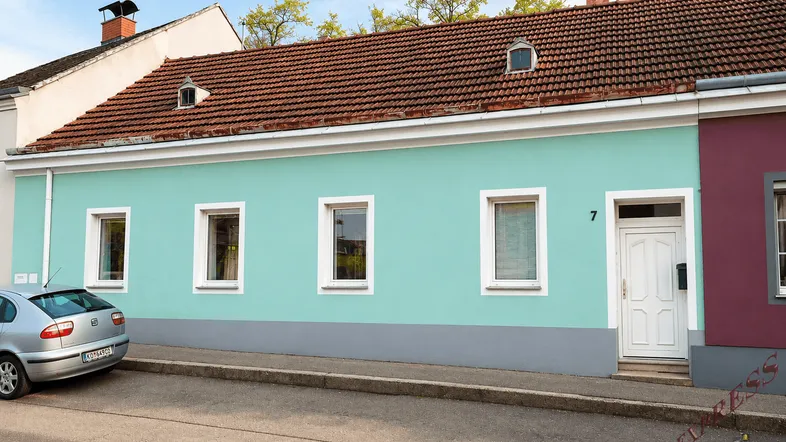 Charmantes Haus mit helltürkiser Fassade, roten Dachziegeln und kleinen Dachgauben.
