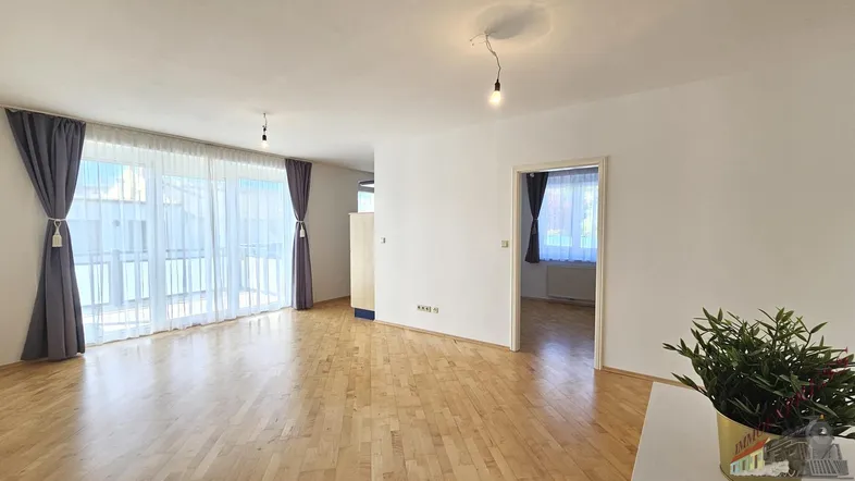 Helles Wohnzimmer mit Parkettboden, weißen Wänden und Zugang zu einem Balkon.