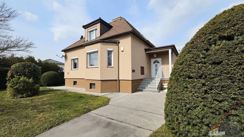 Einfamilienhaus mit gepflegtem Vorgarten und Zufahrt unter blauem Himmel.
