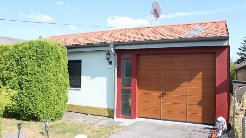 Vorderansicht des Hauses mit Garagentor, Einfahrt und gepflegter Hecke unter blauem Himmel.