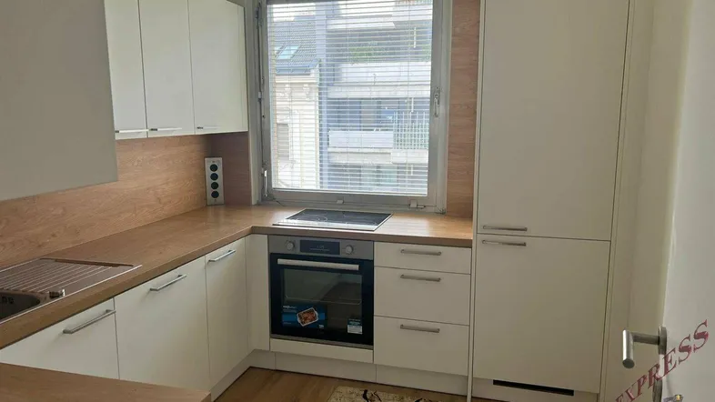 Helle Küche mit weißen Schränken, Holz-Arbeitsplatten und integrierten Geräten sowie Fenster.